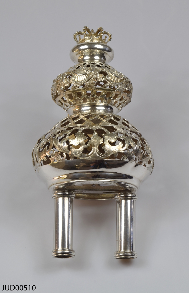 Torahkrona, tillverkad av silver, med löstagbara stavar. Genombruten dekor, och dekorerad med krona på toppen.