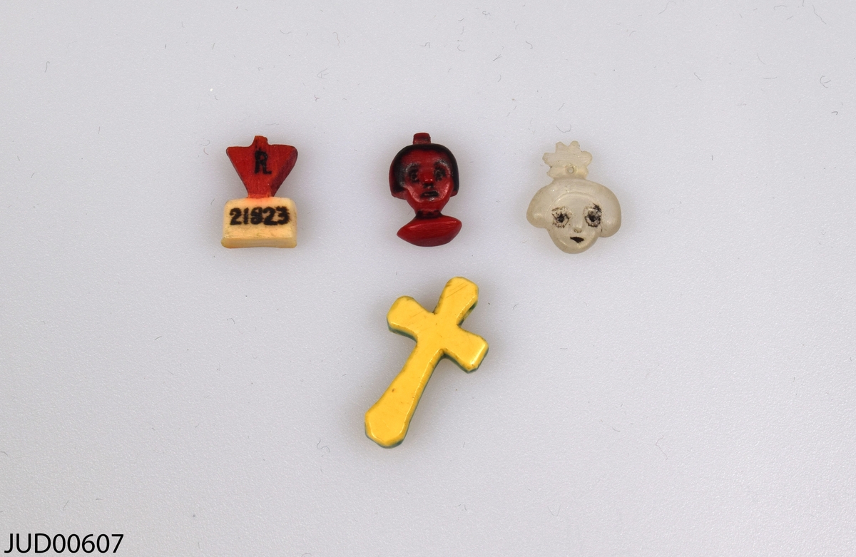 Fyra små figurer täljda från tandborstskaft. Två stycken i form av huvuden, ett i form av ett kors och en sista i form av nummerbricka.