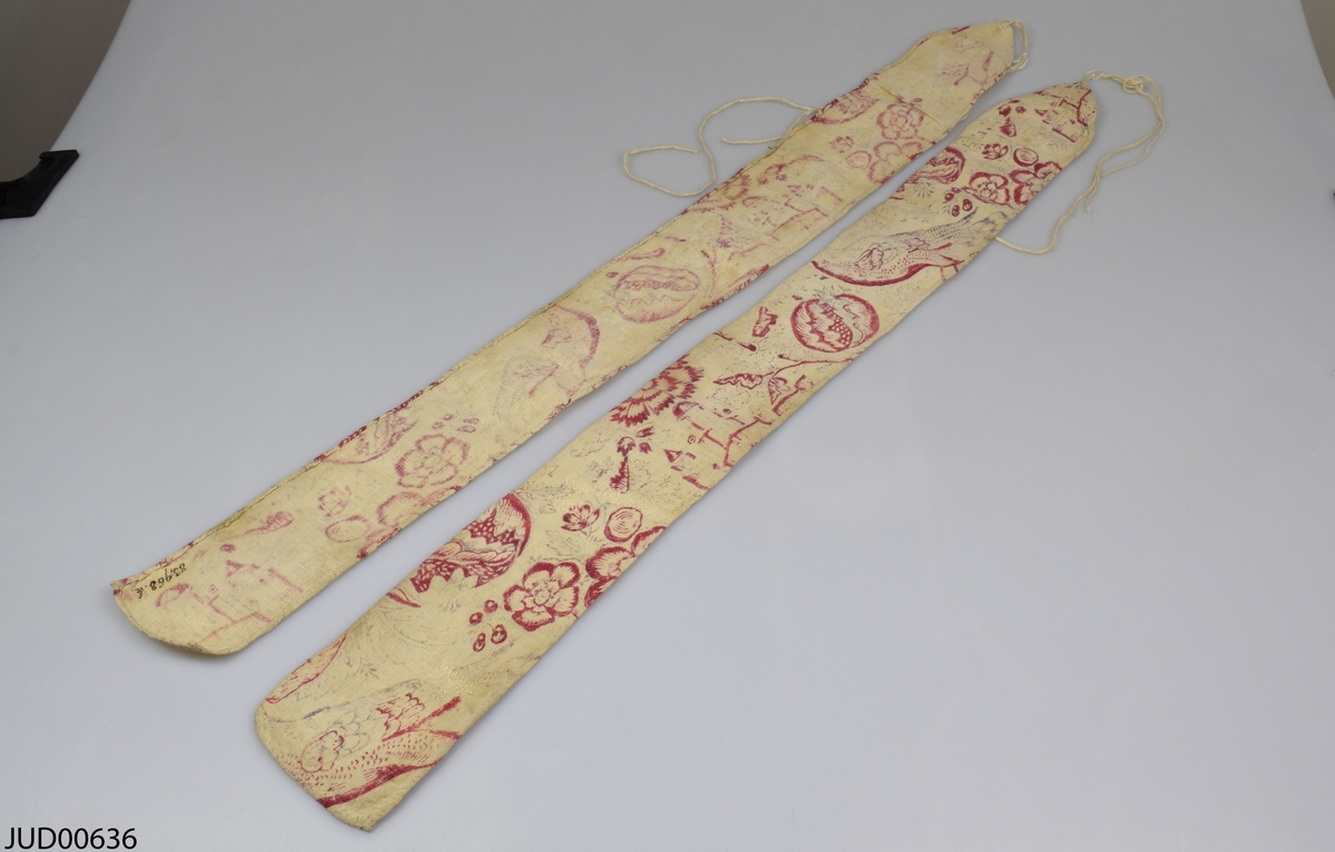 Två långa tygstycken med rött blomstermotiv på vit botten, med snöre i ena änden.
