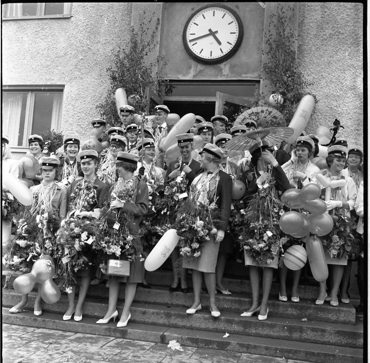 Realexamen i Gränna. Studenter, med blommor och ballonger, uppställda framför skolbyggnaden.