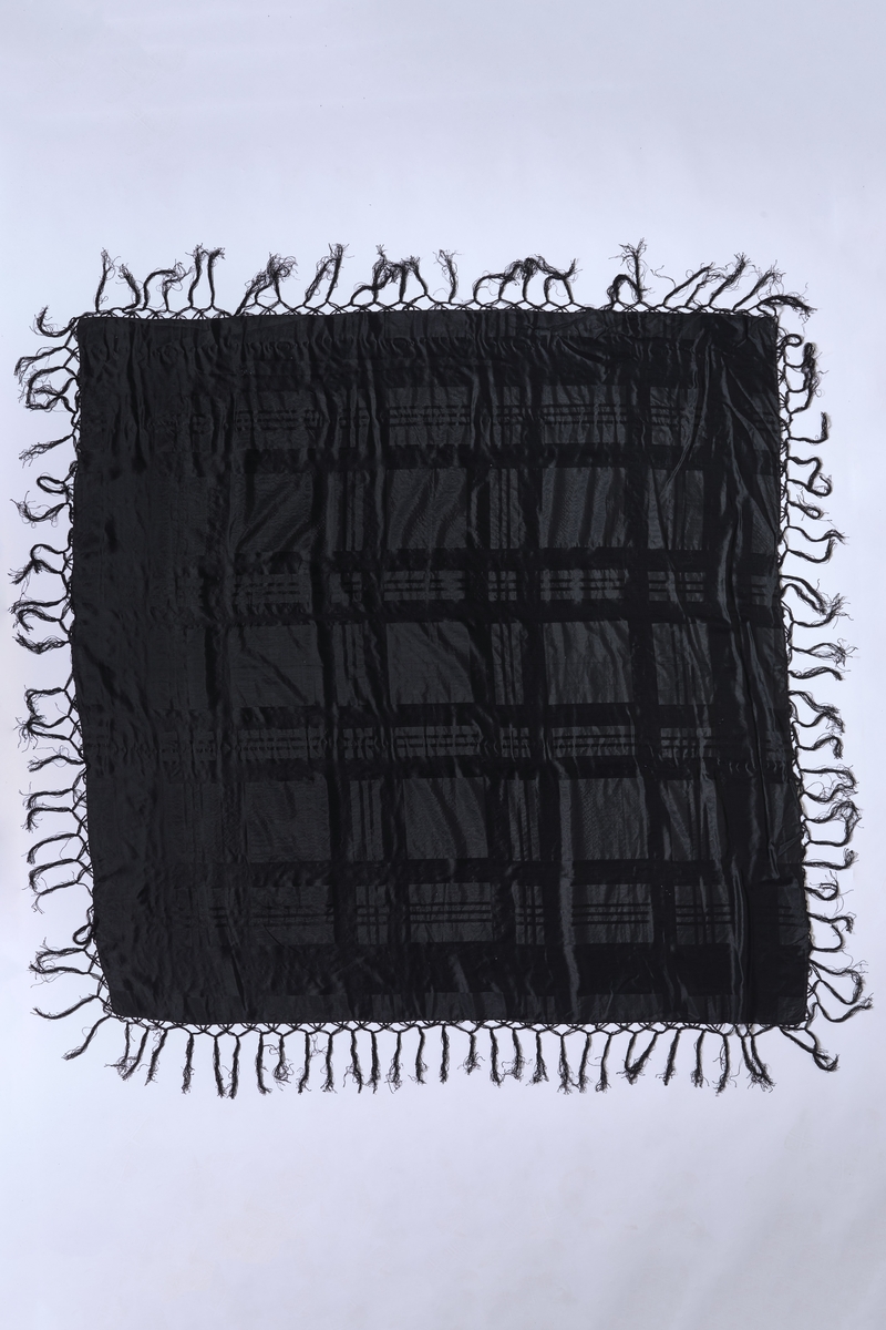 Stort, svart silkesjal med vevet mønstring av sateng i striper /ruter, samt smalere striper i ripsveving. Jarekant i to av sidene, de to andre er faldet for hånd. 