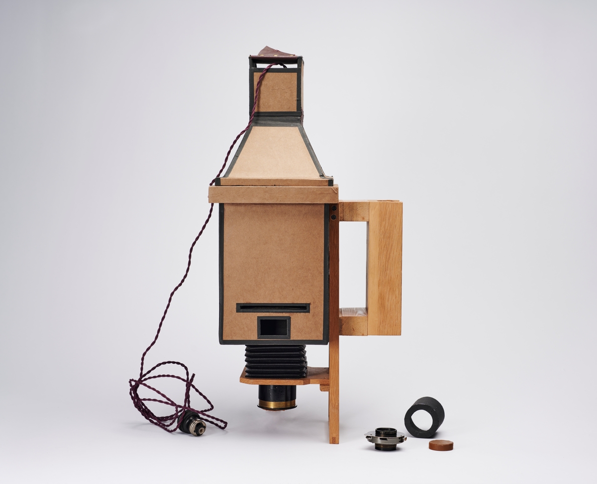 Forstørrelsesapparat laget av arkitekt H. Grendahl (1877-1957). Apparatet har avtagbar lyskilde og objektiv med objektivhette. 
Det følger også med en sort pappsylinder som plasserer like innenfor objektivet og hindrer lyset i å bli spredt.
