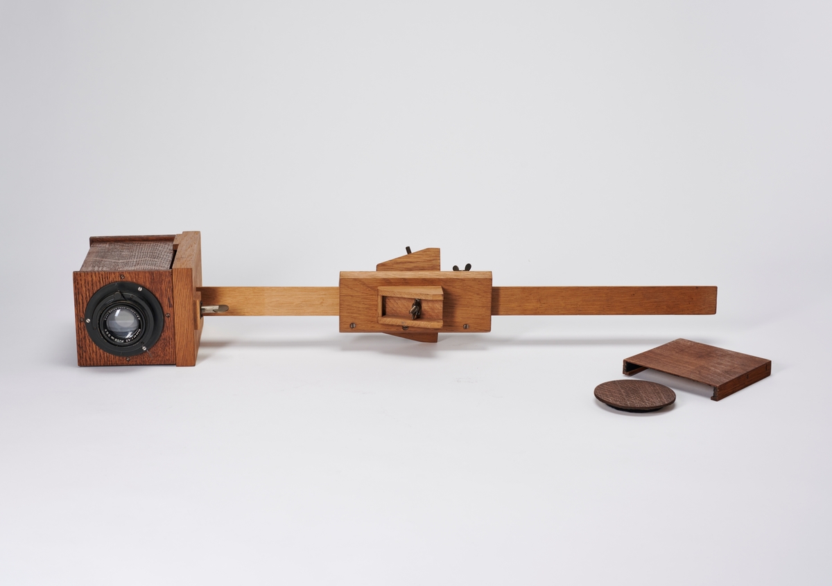Bokskamera med objektiv, mattskive og stativ (mangler ben og kamera mangler en plateholder). Kamera er bygget av arkitekt Hans Grendahl (1877-1957). 
Objektivet er et Carl Zeiss Jena Tessar 1:45 F=18cm DRP.
