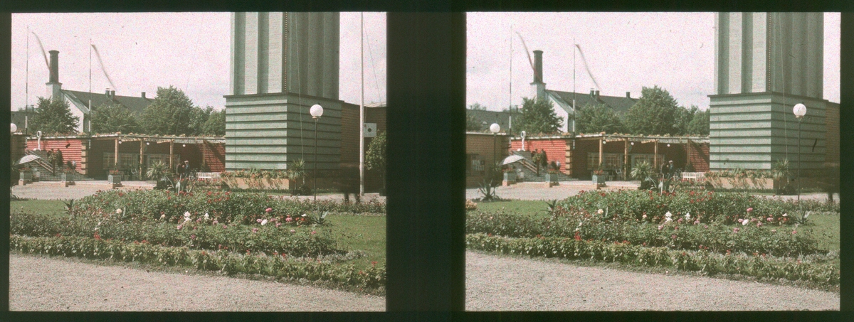 Plass med plantede blomster og palmer, bygd som en del av Drammensutstillingen for å vise frem byutvikling og arkitektur. Nedre del av et tårn. Tilhører Arkitekt Hans Grendahls samling av stereobilder.