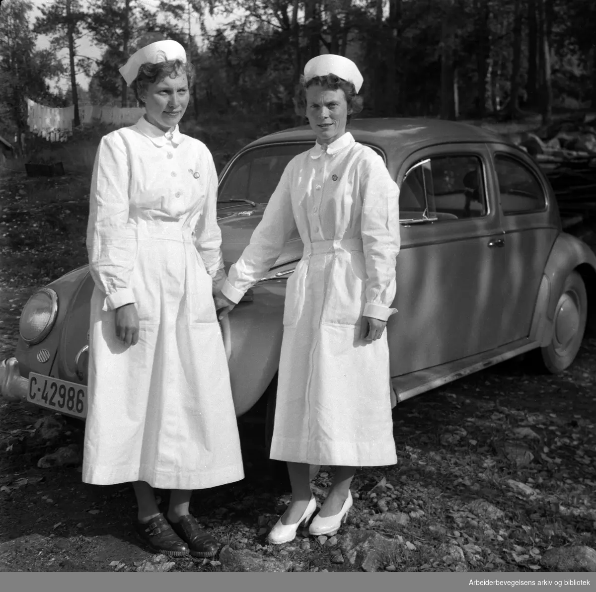 "Helsesøstrene i Nes på Romerike, Ingerid Høye og Valborg Wetrhus foran søster Valborgs bil." September 1957.