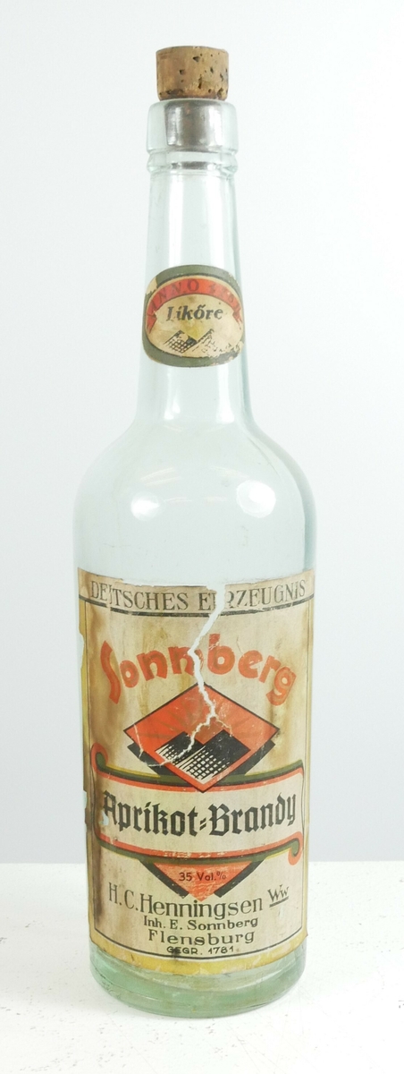 Klar glassflaske med hals som er tettet med en kork. En påklistret etikett på den ene siden og på flaskehalsen. 

Påskrift, etikett, flaskehals: 
Anno 1781 // LIKÓRE

Påskrift, etikett, flaske: 
DEUTSCHES ERZEUGNIS //Sonnberg // Apricot - Brandy  // 35% // H.C HENNINGSEN Ww // Inh. E. Sonnberg // Flensburg // GEGR 1781