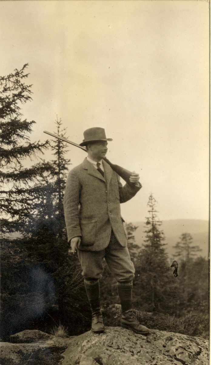 Fritz M. Treschow avbildet på toppen av Rasenakselen(?) med jaktvåpen over skuldrene og sigarett i hånden, antagelig ved Rasensjøene i Stange i Hedmark. Fotografert 1917.