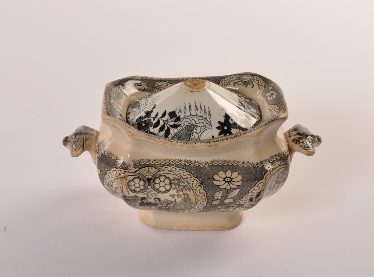 Urneformet avlang terrin i keramikk med 2 hanker og lokk. Krem hvit med sort trykt dekor.  Mennesker og blomster dekor.