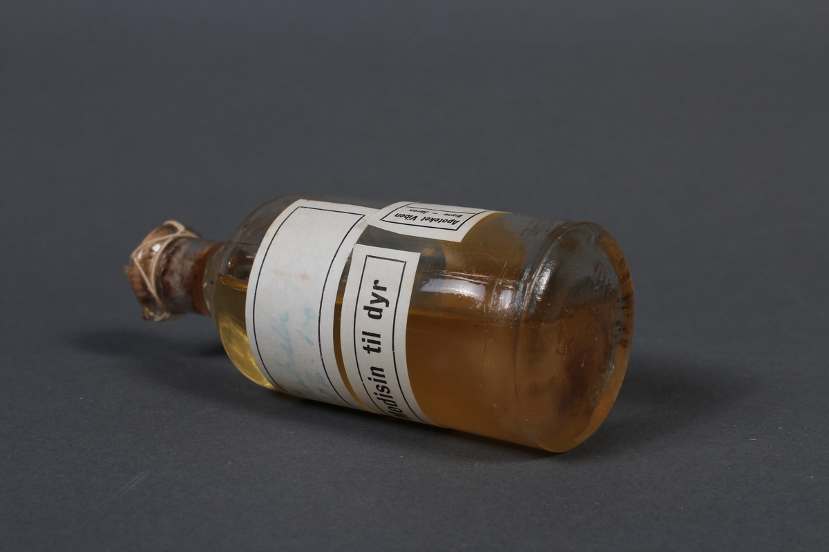 Flaske i klart glass, med kork og etikett. Flasken inneholder gul væske. 
Gjenstanden har vore brukt i samband med dyrlegearbeid på Jæren.