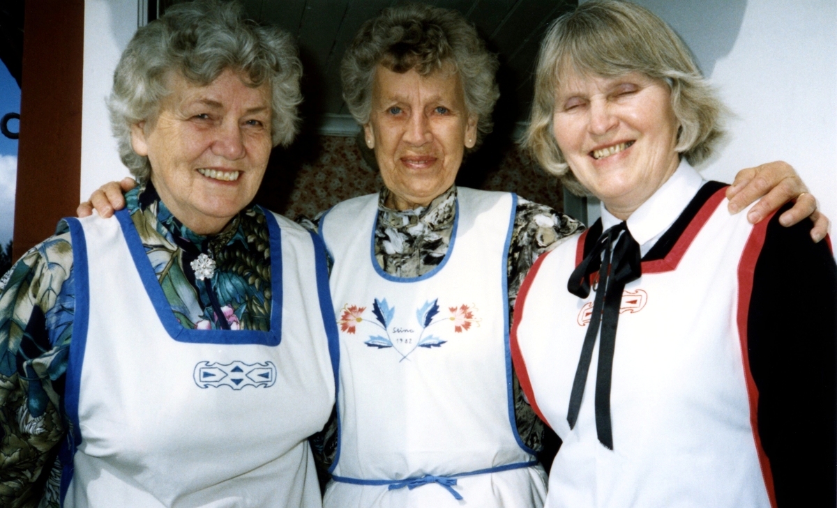 Tre kvinnor iklädda förkläde, står vid ingången till boningshuset Hembygdsgården Långåker 1:3, 1980-tal. Från vänster: Inga-Maj Carlsson (1920 - 1999, Vommedal), Stina Svensson (1912 - 2001, Vommedal) och Emy Johansson (Torrekulla).