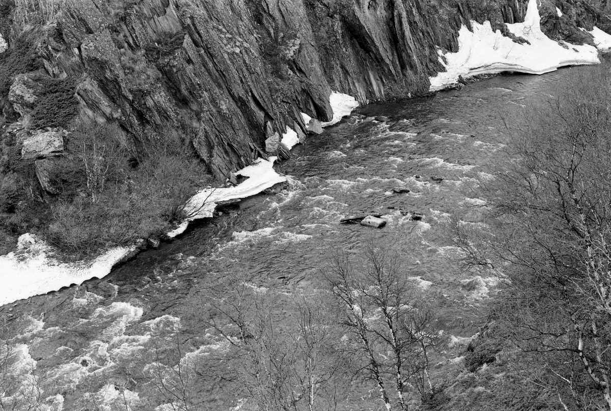 Fossestryk i elva Grimsa i Folldal, fotografert våren 1961. Fotografiet er tatt fra en bergnabb ned mot elveleiet, som her gikk i et gjel som må ha vært vanskelig tilgjengelig for tømmerfløterne. Fotografiet later til å være tatt tidlig på våren, mens det ennå lå litt is langs den ene elvebredden og før det kom lauv på de krokvokste bjørketrærne i den bratte elveskråningen til høyre i forgrunnen på bildet.