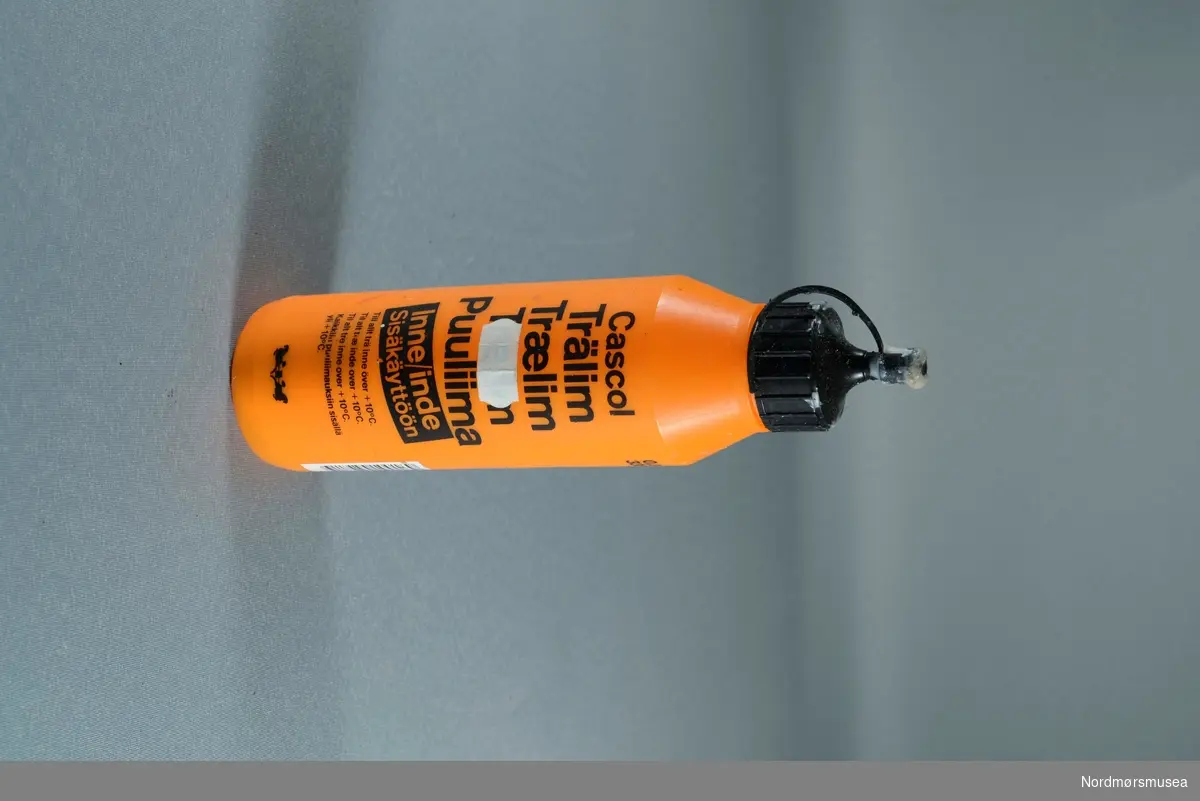 Sylinderformet oransje flaske med sort skrift og topp. Produktinnformasjon på finsk, svensk og dansk.
