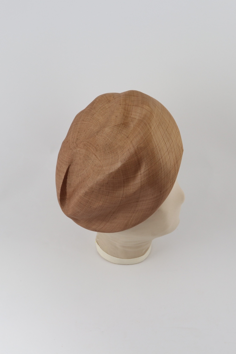 Brun hatt med brettet brem forann og påsydd remse med tvinnet tekstil ved bretten.