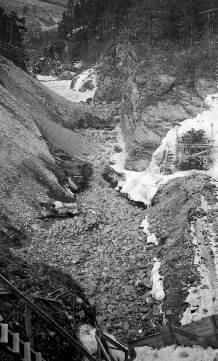 Fra Vinstra, ei sideelv til Gudbrandsdalslågen i Nord-Fron kommune i Midt-Gudbrandsdalen. Fotografiet er tatt fra krona på kraftverksdammen ved Kamfossen, ved utløpet av Olstappen i Skåbu. Vi ser ned i et tørrlagt elveleie. Bildet ble tatt i 1954, etter at det var støpt ny dam ved Kamfossen.