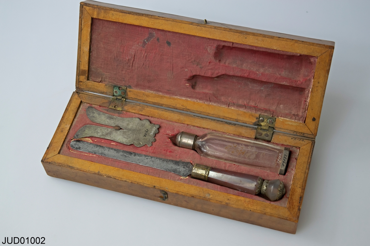 En klädd träask med tre föremål för omskärelsen: kniv, sköld och flaska för blodstillande medel.