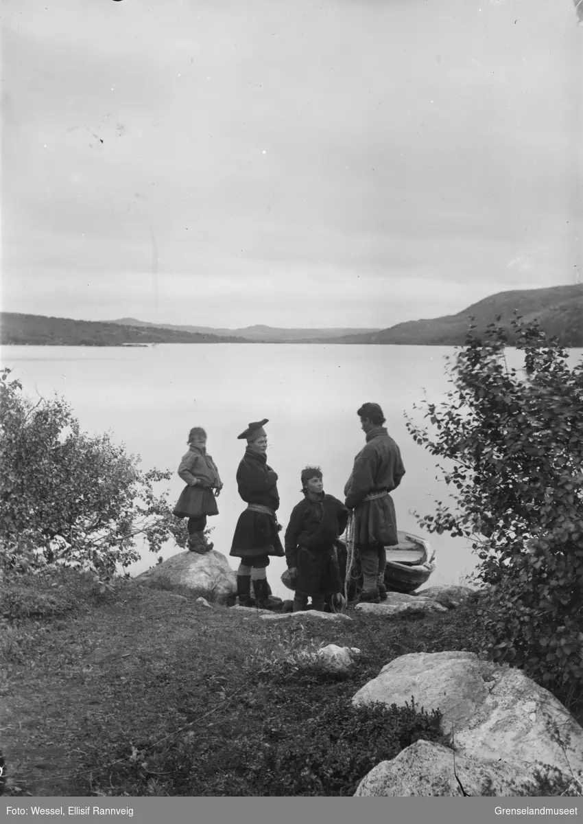 En robåt i vannkanten ved Førstevannet, Kirkenes. Utsikt sørover. Fire unge gutter står på land. Fra venstre på en stein Mattis Pak, Samuel ? med stjernelue, Ole Pak og Jon Pak.