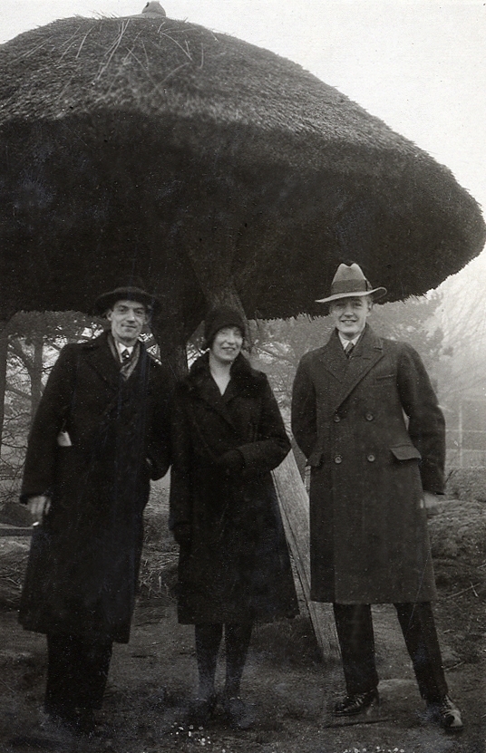 En kvinna och två män står vid ett vasstäckt "parasoll" vid caféet Villa Utsikten i Karlshamn. 
Vid fotot text: "Hos Hugo A. 1930".