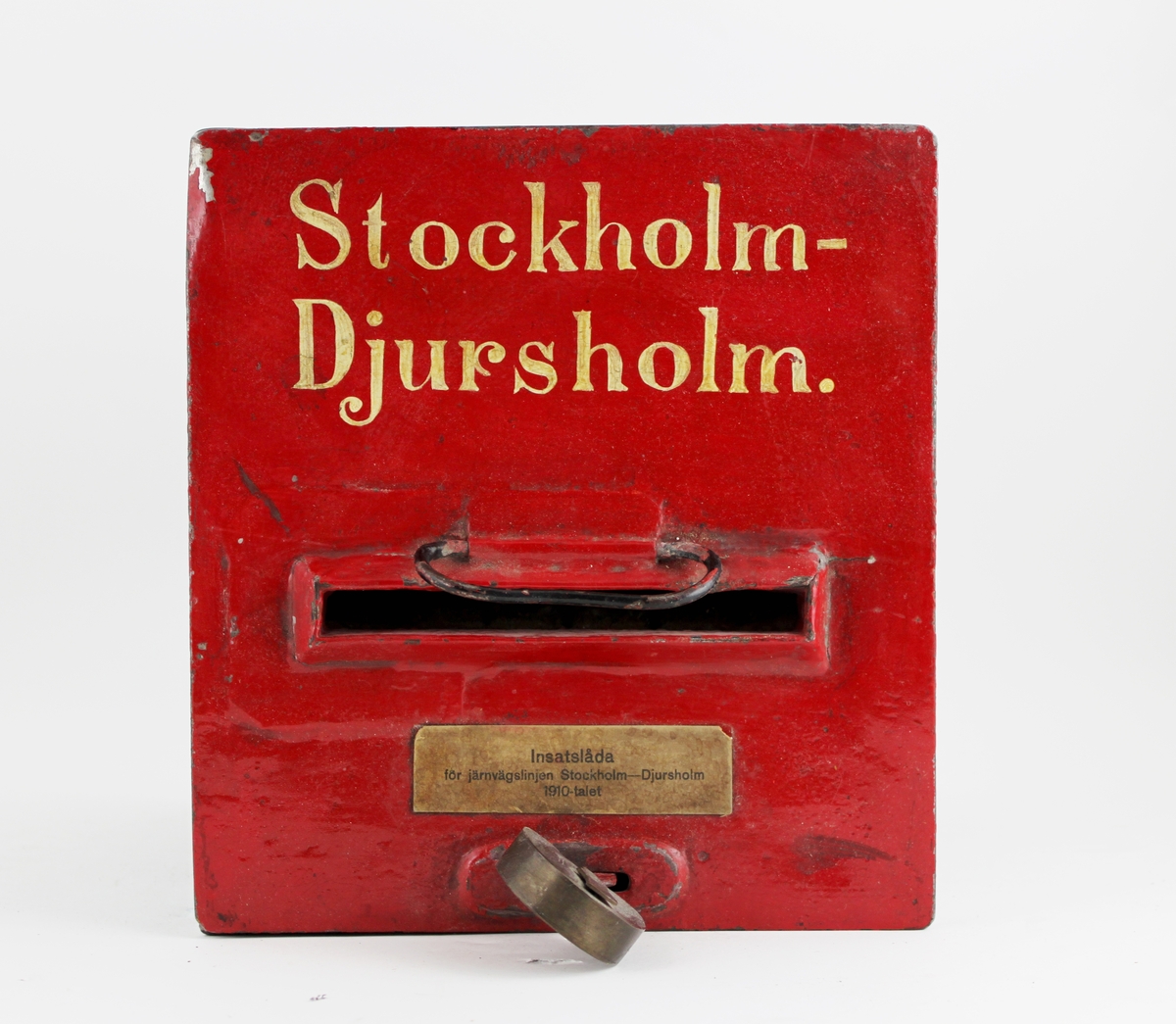 Insatsbrevlåda, svart med rött lock och texten Stockholm
-Djursholm i vitt på locket. Lådan är låst med ett hänglås,
hänglåsetär märkt P.L. (=postlås). Insatsbrevlådor infördes 1868 och
varavsedda för befordran av vanliga brev och brevkort
mellanpostanstalter invid järnvägs- och ångbåtslinjer.