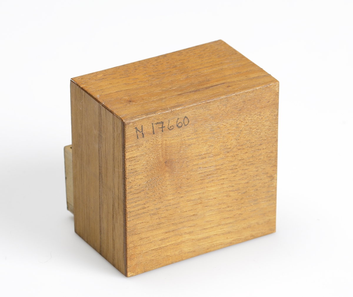 Dockskåpsbyrå i trä. Tre utdragbara lådor med intarsia på lådfronten. I lådorna förvaras tre dockkläningar, två hättor och diverse små tygbitar.