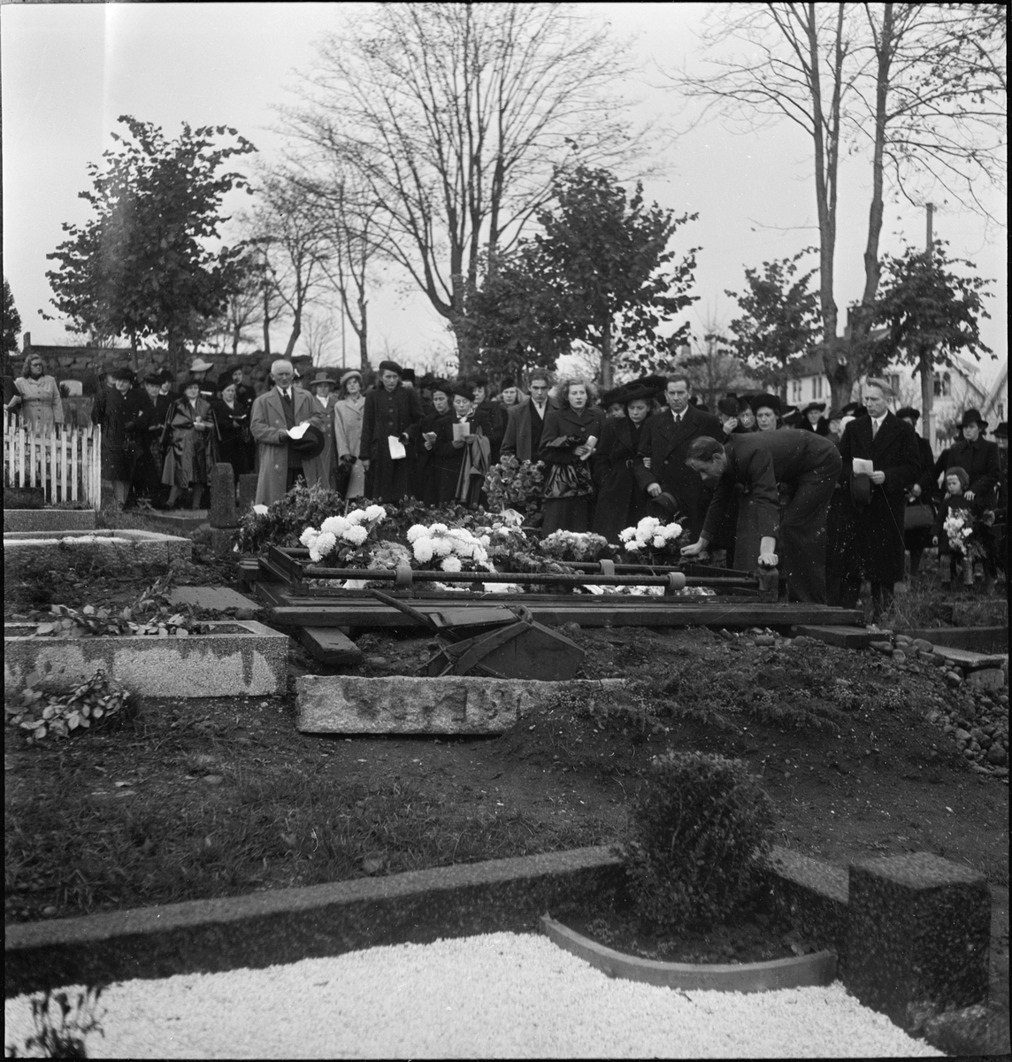Begravelsen til fru Karlsen. En blomsterkledd kiste bæres ut og jordlegges på kirkegården i Egersund.