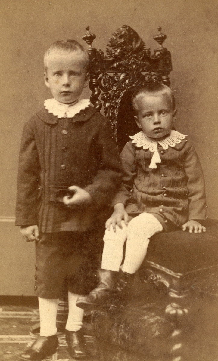 Två små pojkar fotograferade vid en stol.