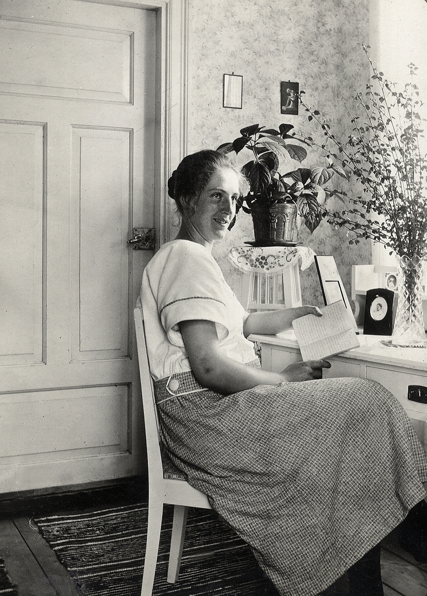 En kvinna i blus och kjol sitter och läser vid ett vitmålat skrivbord.