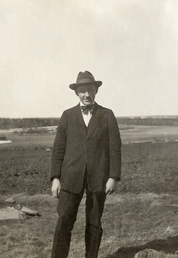 En man i hatt och kostym poserar vid en åker.