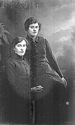 Två kvinnor i frälsningsarméns uniform. En sitter i en stol och den andra på dess armstöd.
