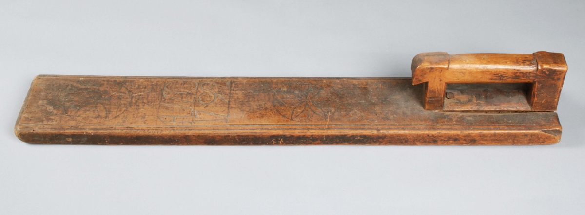 Mangelbräde i brunbetsat trä (färgslitage). Infällt, rakt, skuret handtag på ena änden, i form av stiliserad häst. Brädet avlångt, med dubbelprofilerade kanter på långsidorna. Mittpartiet med skuren dekor, i form av 2 stora bladrosetter samt årtalet "ANO 1792". Lätt maskstunget.

Mangelbräde eller kavelbräde är ett redskap av trä som använts för mangling av textilier. Mangelbrädet användes tillsammans med en kavel, en slät rulle av trä. Den textil som skulle manglas, rullades upp på kaveln, på ett bord eller annat slätt underlag. Under hårt tryck, rullades kaveln med hjälp av mangelbrädet, fram och tillbaka över bordet. (Wikipedia)