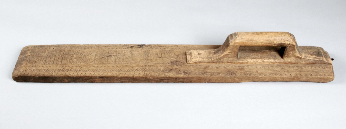 Mangelbräde i brunbetsad ek (färgslitage). Handtaget i björk? med lång, infälld fot. Ovansidan med skuren dekor i form av zigzag-linjer, rutor och rosetter, samt "ANNO 1786 BED". 

Mangelbräde eller kavelbräde är ett redskap av trä som använts för mangling av textilier. Mangelbrädet användes tillsammans med en kavel, en slät rulle av trä. Den textil som skulle manglas, rullades upp på kaveln, på ett bord eller annat slätt underlag. Under hårt tryck, rullades kaveln med hjälp av mangelbrädet, fram och tillbaka över bordet. (Wikipedia)