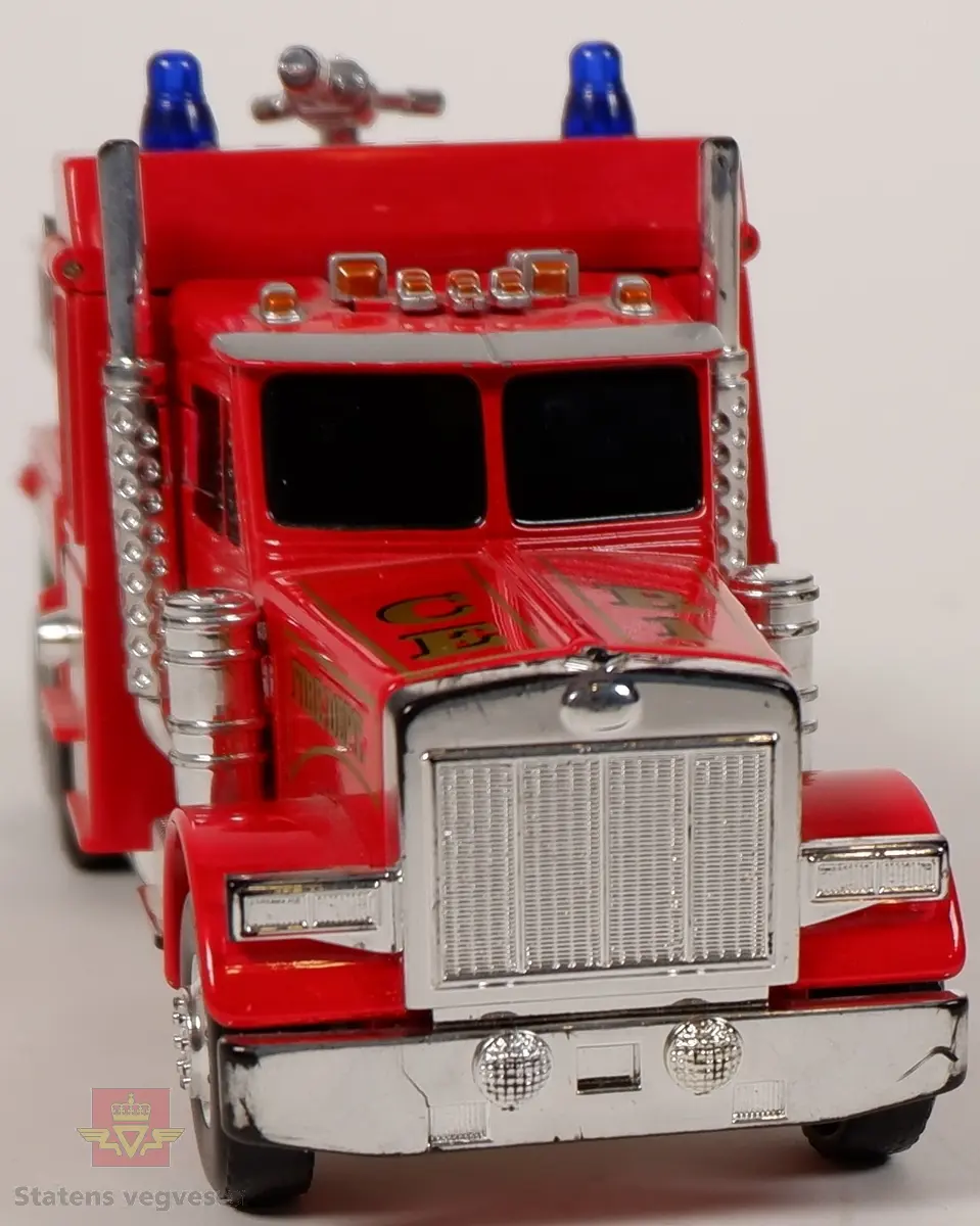 Miniatyrlastebil utformet som brannbil. Lastebilen kan brettes ut slik at det blir en lekefigur. Fargen er rød med påskrifter i gull, detaljer i sølv og to blå blinklamper på taket. Miniatyren er laget av plast og metall.