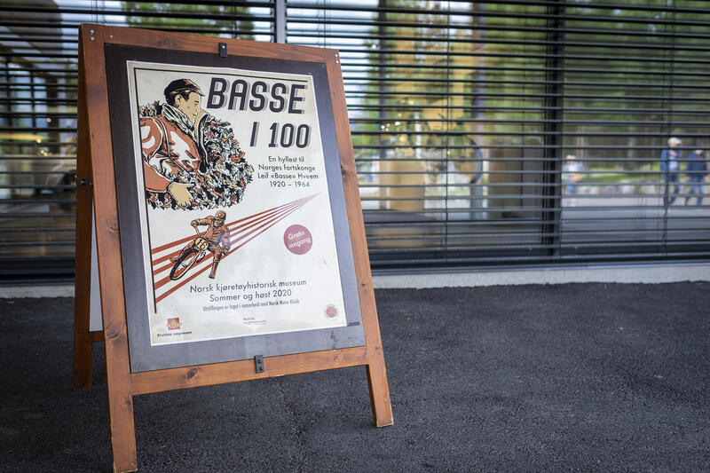 Plakat til utstillingen Basse i 100 på en plakatbukk utenfor Norsk kjøretøyhistorisk museum.