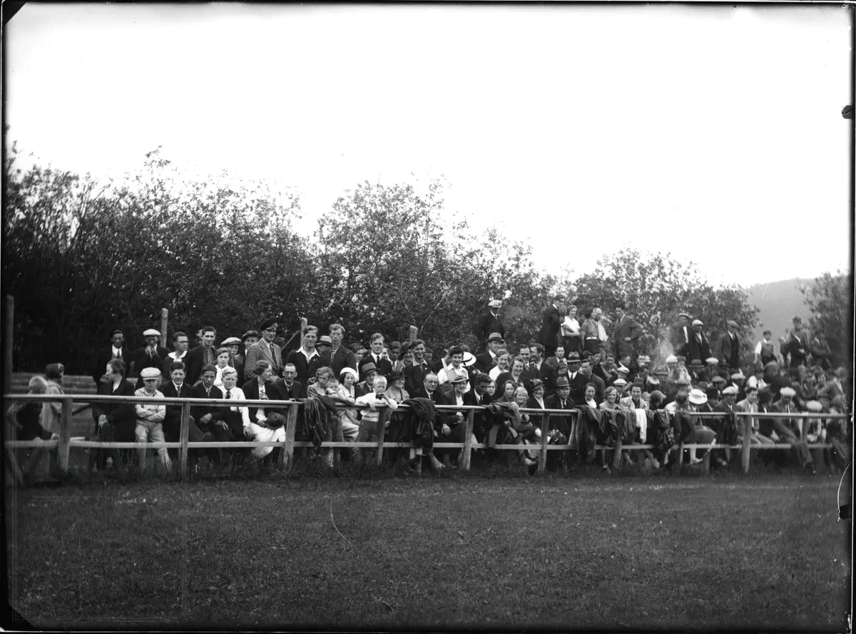 Publikum sitter og står ved en idrettsplass/fotballbane.