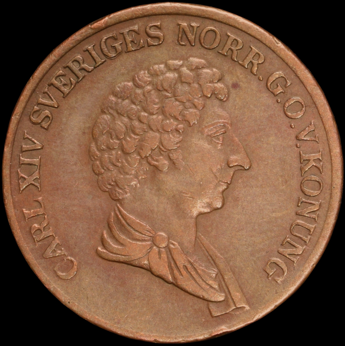 Mynt med valören 1 skilling banco. Åtsidan har en bild på Kung Karl XIV Johan. Frånsidan visar valören, två korslagda pilar samt en växtkrans.
