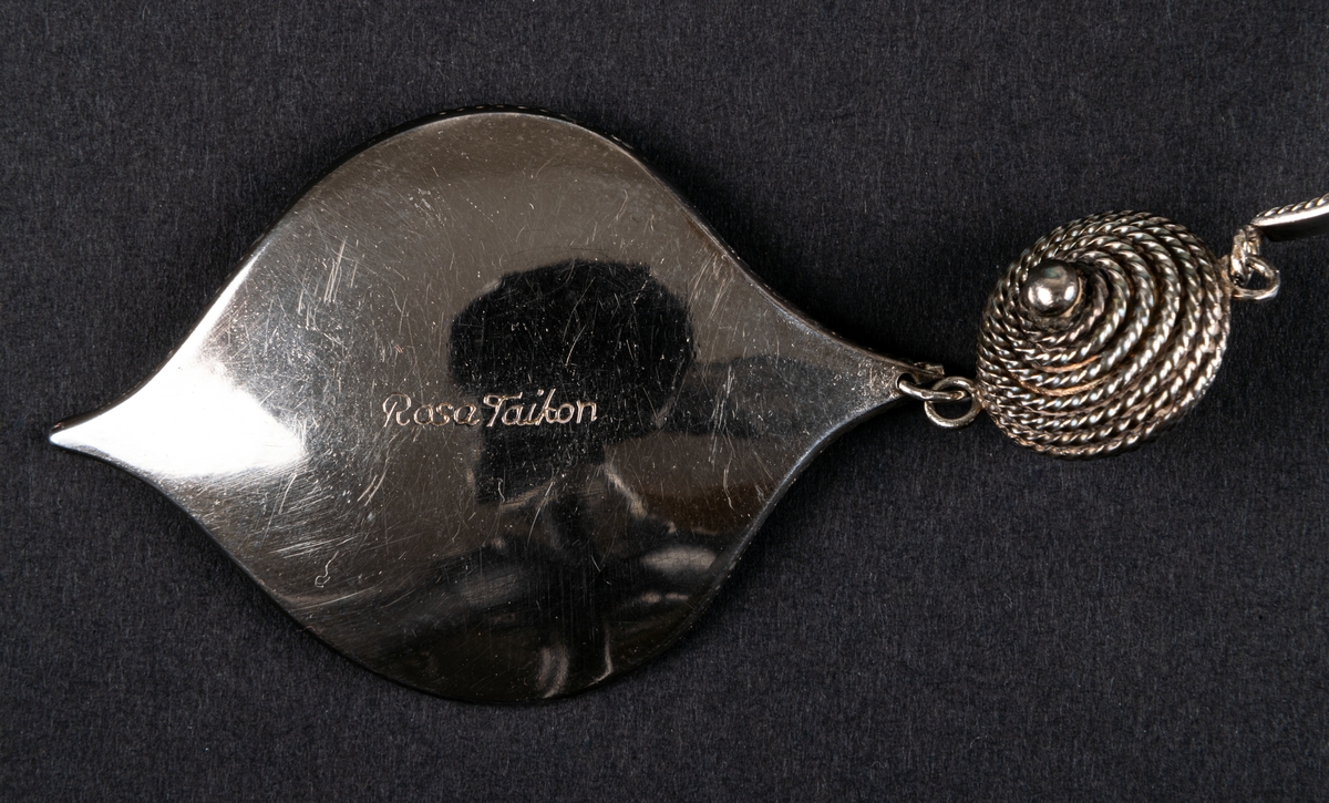 Ashwa, smycke i silver av Rosa Taikon.
Öronsmycke i form av två silverlöv med granalieornamentik, vilka via varsin granelerad kula hänger i en dubbel bygel att sätta över huvudet.