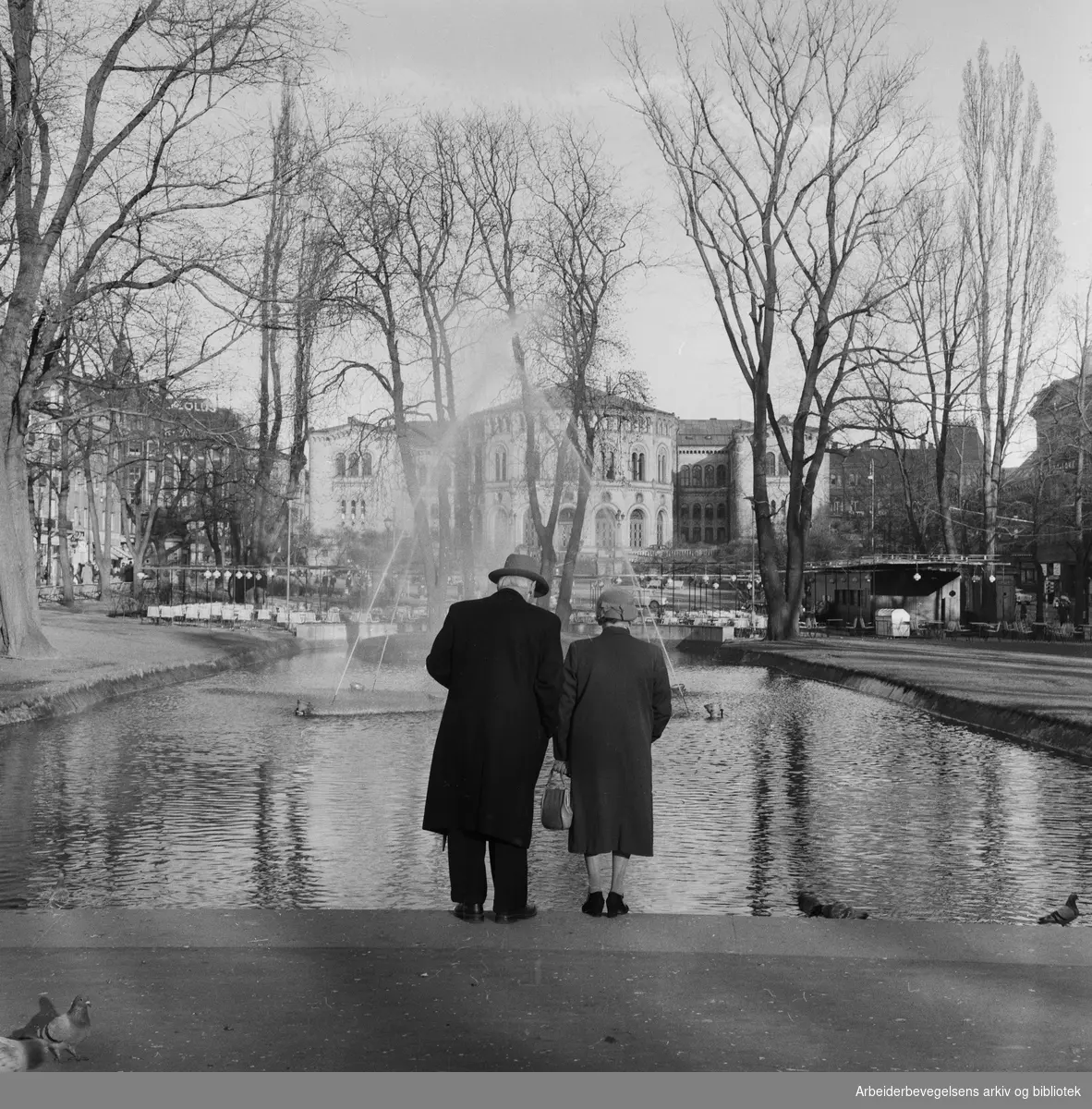 Eldre par ved fontenen i Spikersuppa. Stortinget i bakgrunnen. April 1960.