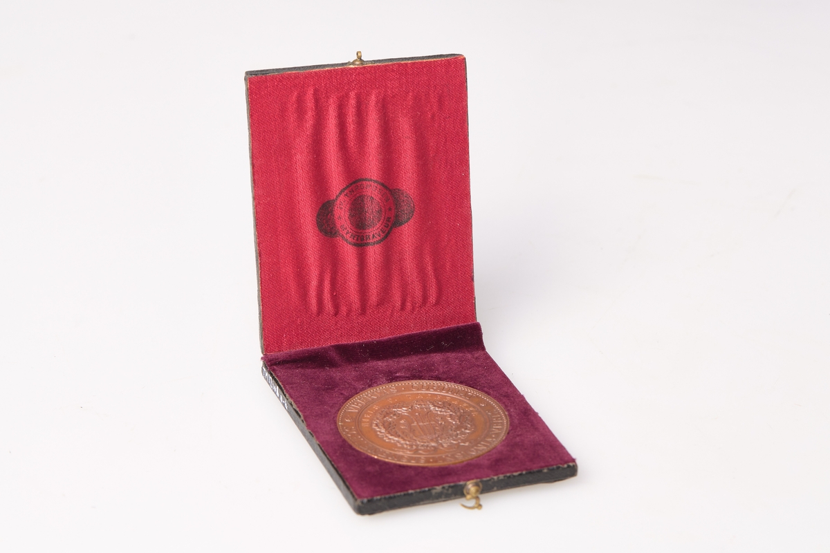 Pris fra en utstilling eller konkurranse avholdt i 1891. Medaljen har inskripsjon på den ene siden: DEN ALMINDELIGE NORSKE LANDBRUKSUDSTILLING I SKIEN 1891, på den andre siden: VBERTAS CORONAT - SCHIENENSIS INSIGNIA VRBIS, samt inngravert: Niels P Talebakke. Medaljen er av bronse og er produsert av Iv. Throndsen myntgraveur.