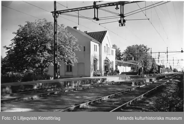 Spårområde vid Långås järnvägsstation. Väntande människor på perrongen, både sittande och stående.