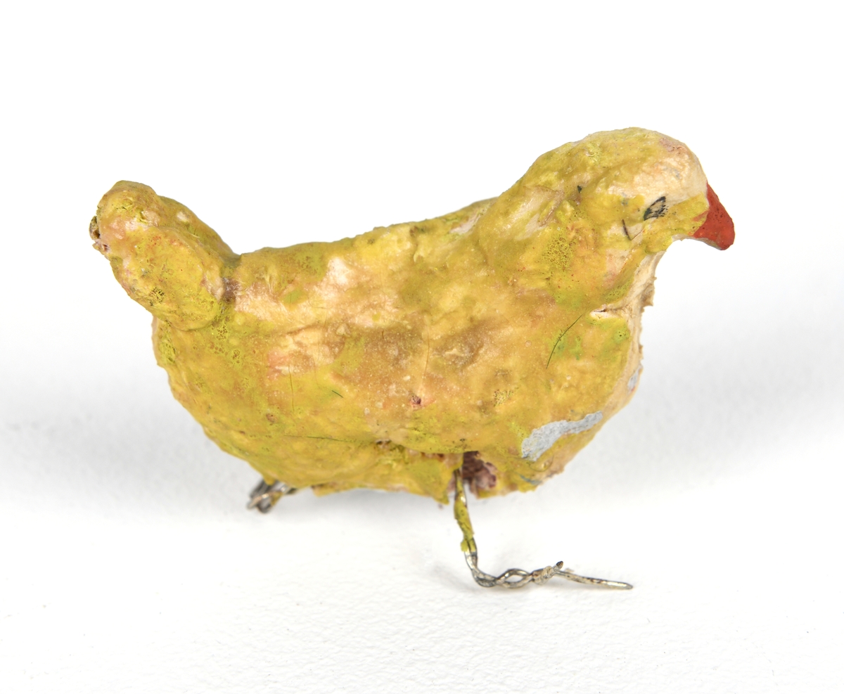 En høne av pappmasje laget av en elev (i formingsfag). Figuren har et skjelett av ståltråd med flere lag papir utenpå. Hønen er malt gul med rødt nebb og detaljer i svart.