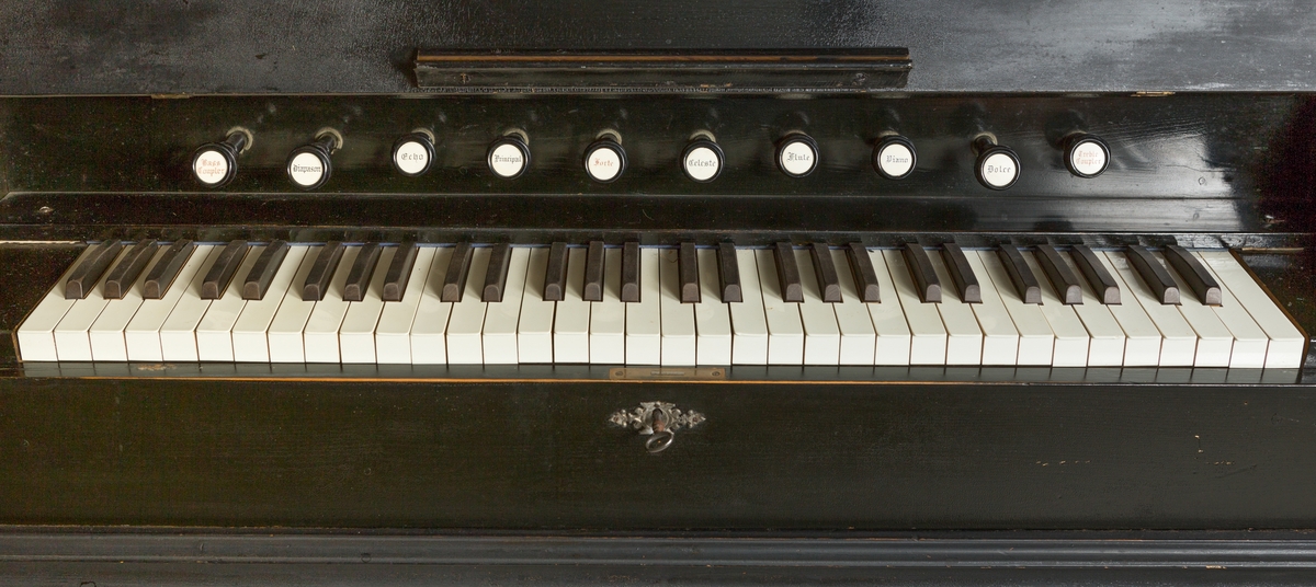 Orgel, pumpeorgel med to messinglysestaker over tangentene. Ett bærehåndtak i messing i hver kortside.