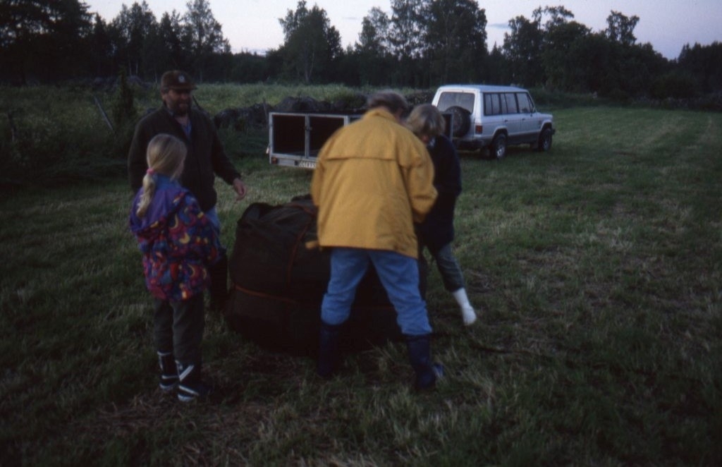 Tre vuxna och ett barn står vid en stor bag. Det är ett ballonghölje som har packats ihop.
