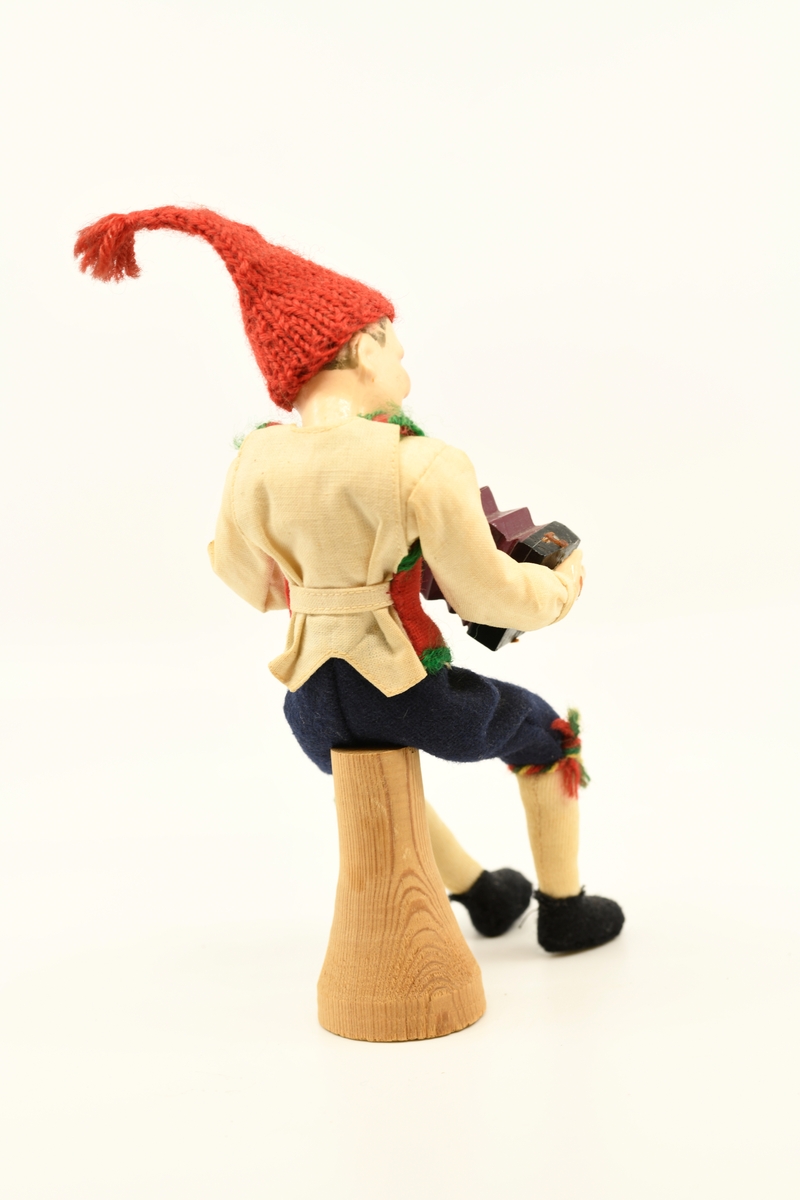 Dukke som forestiller mann som sitter på en "stubbe" og spiller på trekkspill.