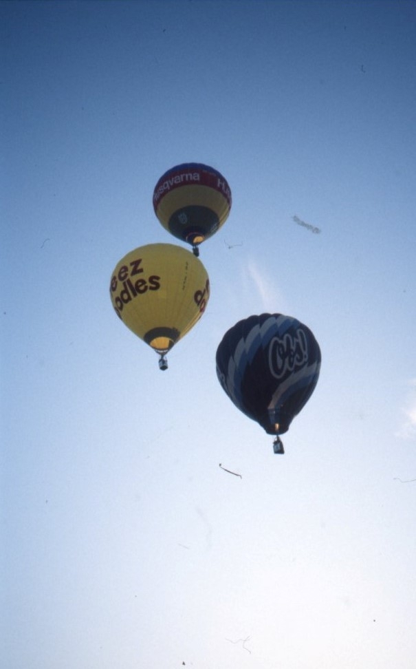 kameran riktas mot himmlen. Tre luftballonger flyger. En blå luftballong med texten Obs! En gul luftballong med texten Cheez Doodles och en röd ballong med texten Husqvarna.