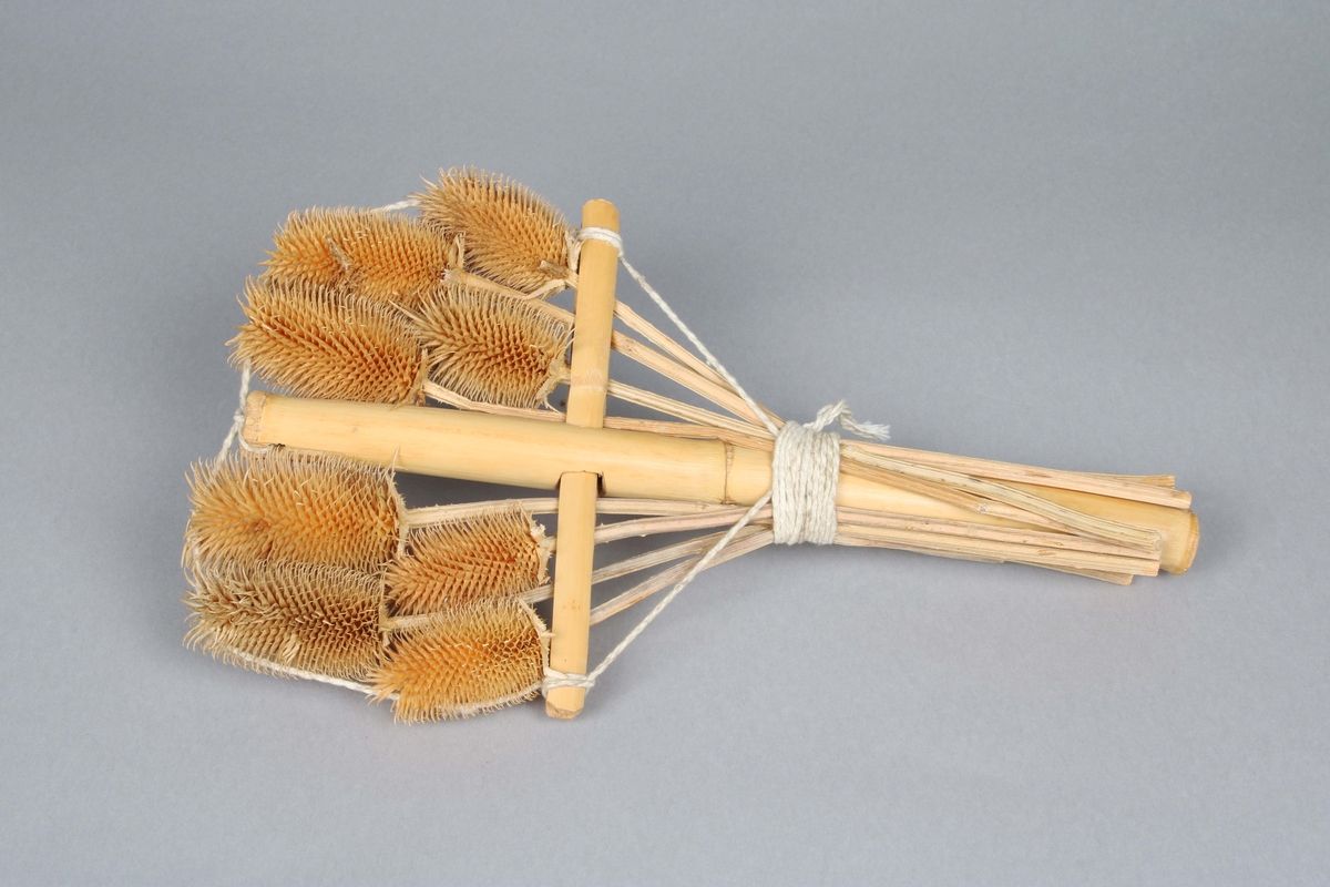 Korsformad ställning av bamburör, på vilken 8 kardborrar med stjälk, bundits fast med bomulls-snöre.

Kardborrar användes tidigare vid maskinell ruggning av kardgarnstyger. Se ruggmaskin BM 46181.

Inköpt i samband med utställningen Mayaindianernas liv 1/18-1976 - 15/2-1976 på Borås Museum.
