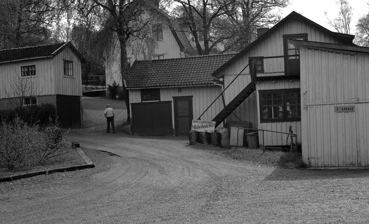 John Lindström Möbelsnickeri vid Ekebacken på Gamla Riksvägen 79 (nu: Gamla Riksvägen 81), 1980-tal. Till vänster ligger Lillstugan. I mitten boningshuset med två lägenheter. Till höger snickeriet med garage. Skylten finns nu i Hembygdsföreningens samlingar. Notera i mitten hur taket har ändrats efter björken. John Lindström promenerar upp mot bostaden.