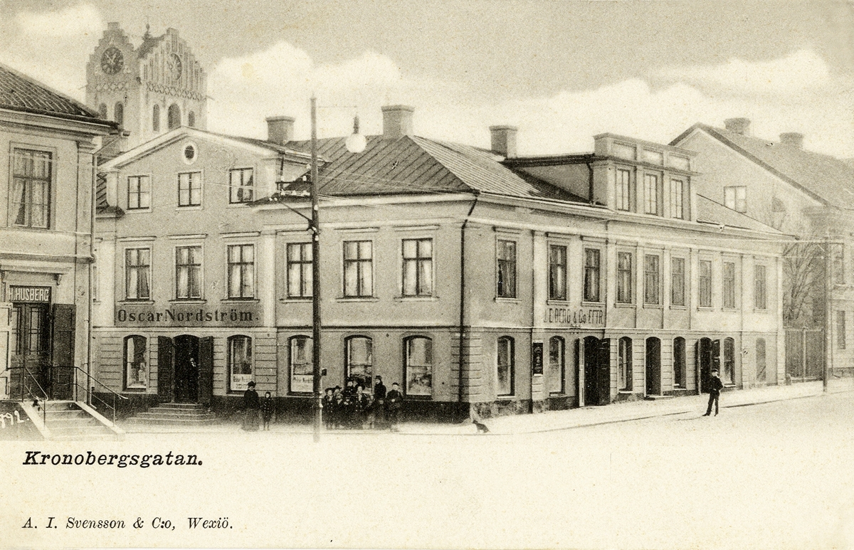 Kronobergsgatan, Växjö, mot sydost, 1900.
Man ser några av husen i kv. Lejonet och bakom dem domkyrkans dåv. torn. Till vänster skymtar också dåv. hörnhuset i kv. Lyktan, som senare ersattes av Riksbankshuset.