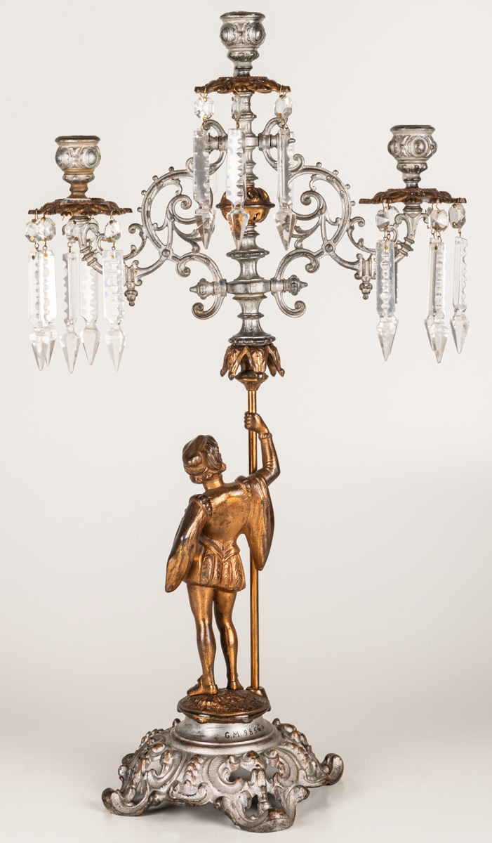 Kandelaber, en i ett par, av bronserat järn, tre ljuspipor med prismor.

