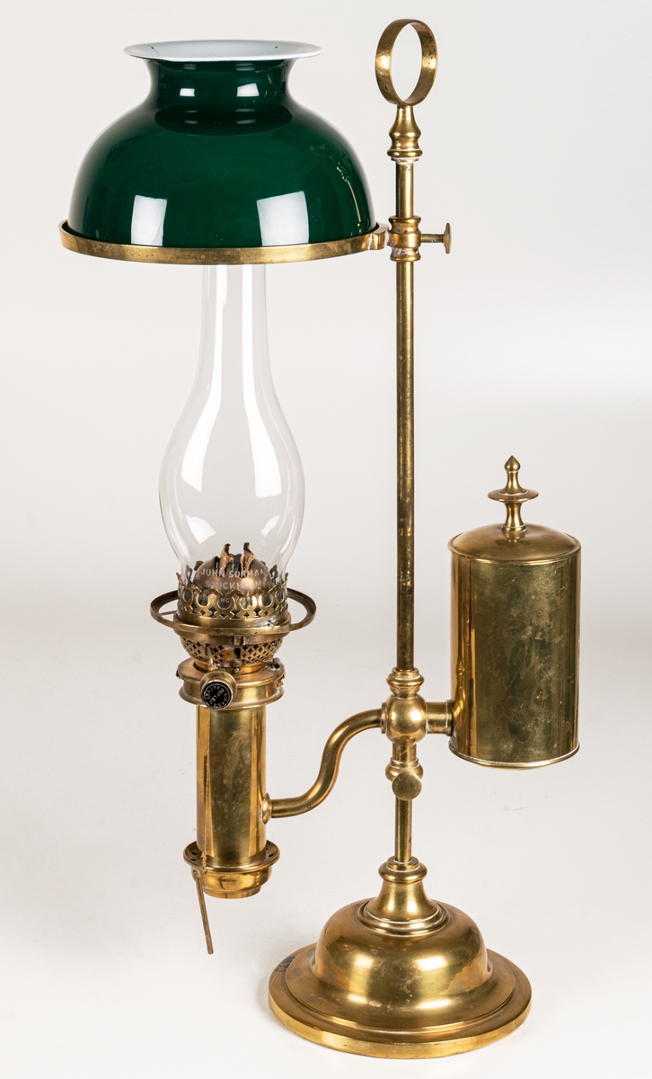 Bordslampa, av mässing, med grön porslingskupa. Hinks & sons patent.
På brännglaset John Surman, Stockholm.