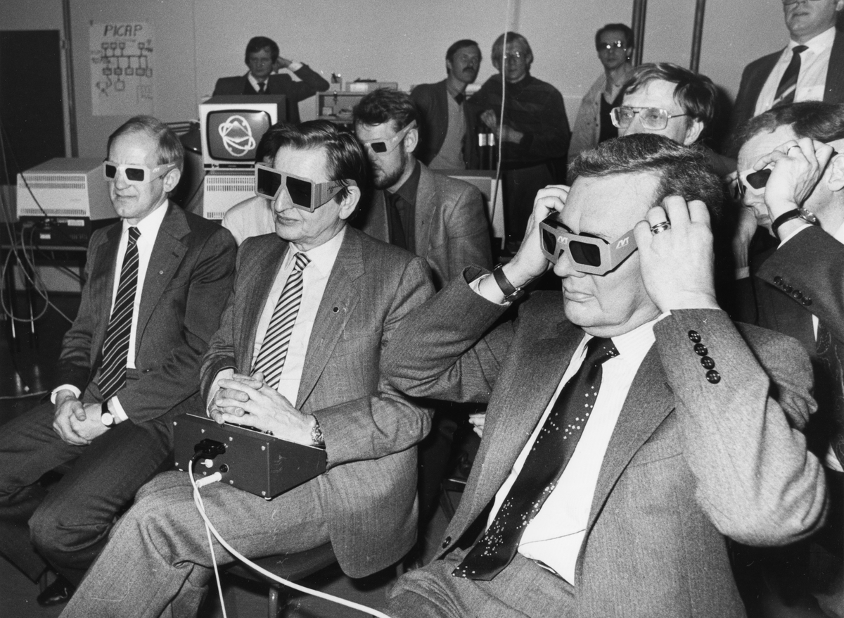 Bild i Cupolen under Tekniska Träffen i Linköping den 17-18 mars 1983. Några män sitter och tittar på TV-apparater utanför bilden iförda 3D-glasögon. I mitten sitter Olof Palme med nån teknisk låda i knät.