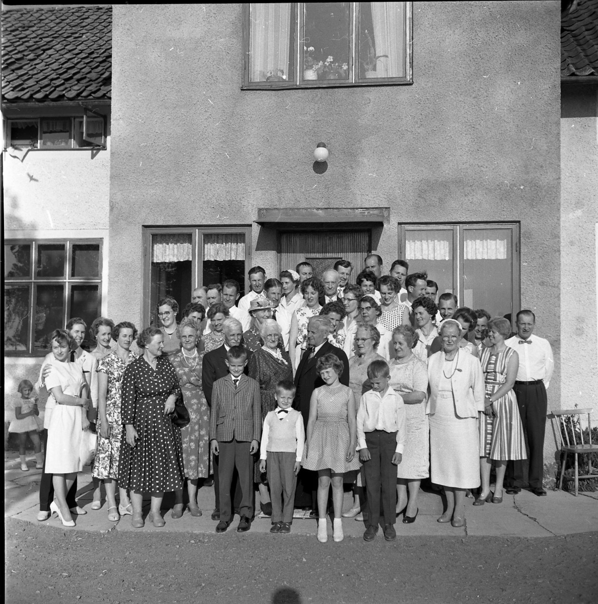 Släktmöte 1960. En stor skara människor, både barn och vuxna står uppställda framför ett hus med putsad fasad.